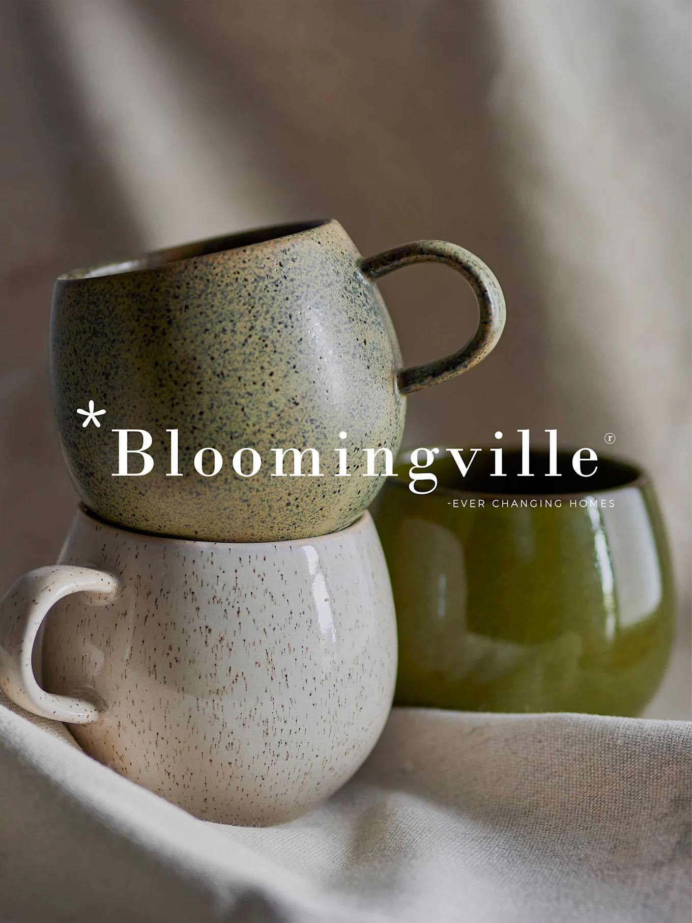 Bloomingville-logotyp över en stapel av två spräckliga keramikmuggar i grönt och benvitt, med en annan enfärgad grön mugg bredvid.