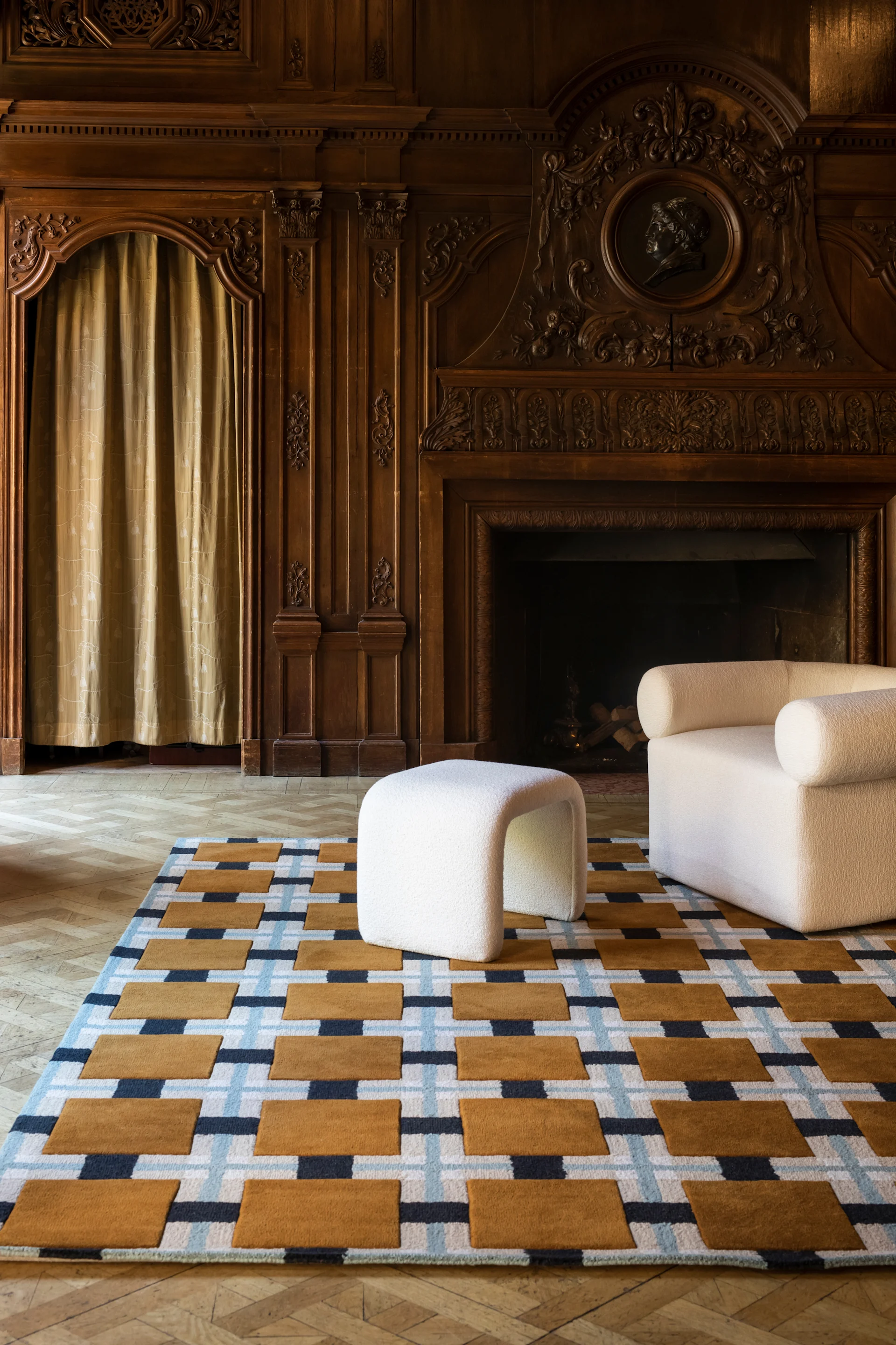 Geometrisk matta med bruna, blå, vita mönster, en vit texturerad ottoman och fåtölj i ett träpanelklätt rum.