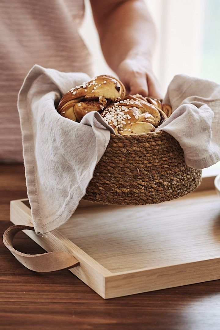 Nybakta bullar serveras ur en flätad brödkorg och vilar på en ljusgrå linneservett från House Doctor. 