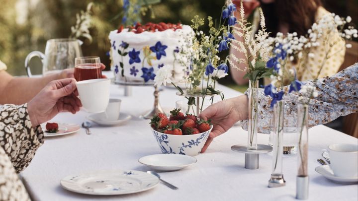 Låt blommor i olika vaser pryda bordet för din blåvita midsommardukning, de blåa blommorna kommer även igen på Havspil skål från Scandi Living, här med jordgubbar i.