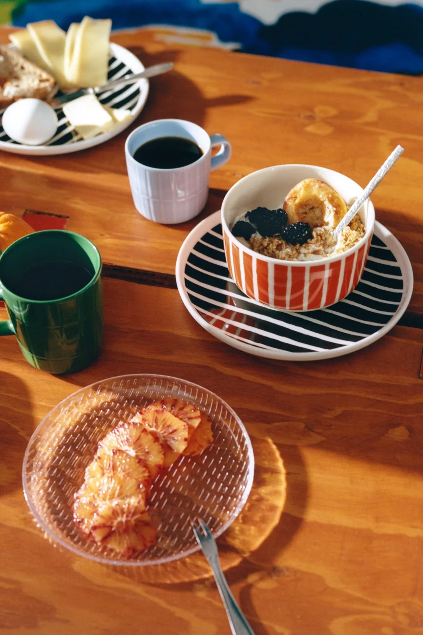 Frukost på träbord med randig servis, kaffe, havregrynsgröt, ost, bröd, ägg och blodapelsinskivor.