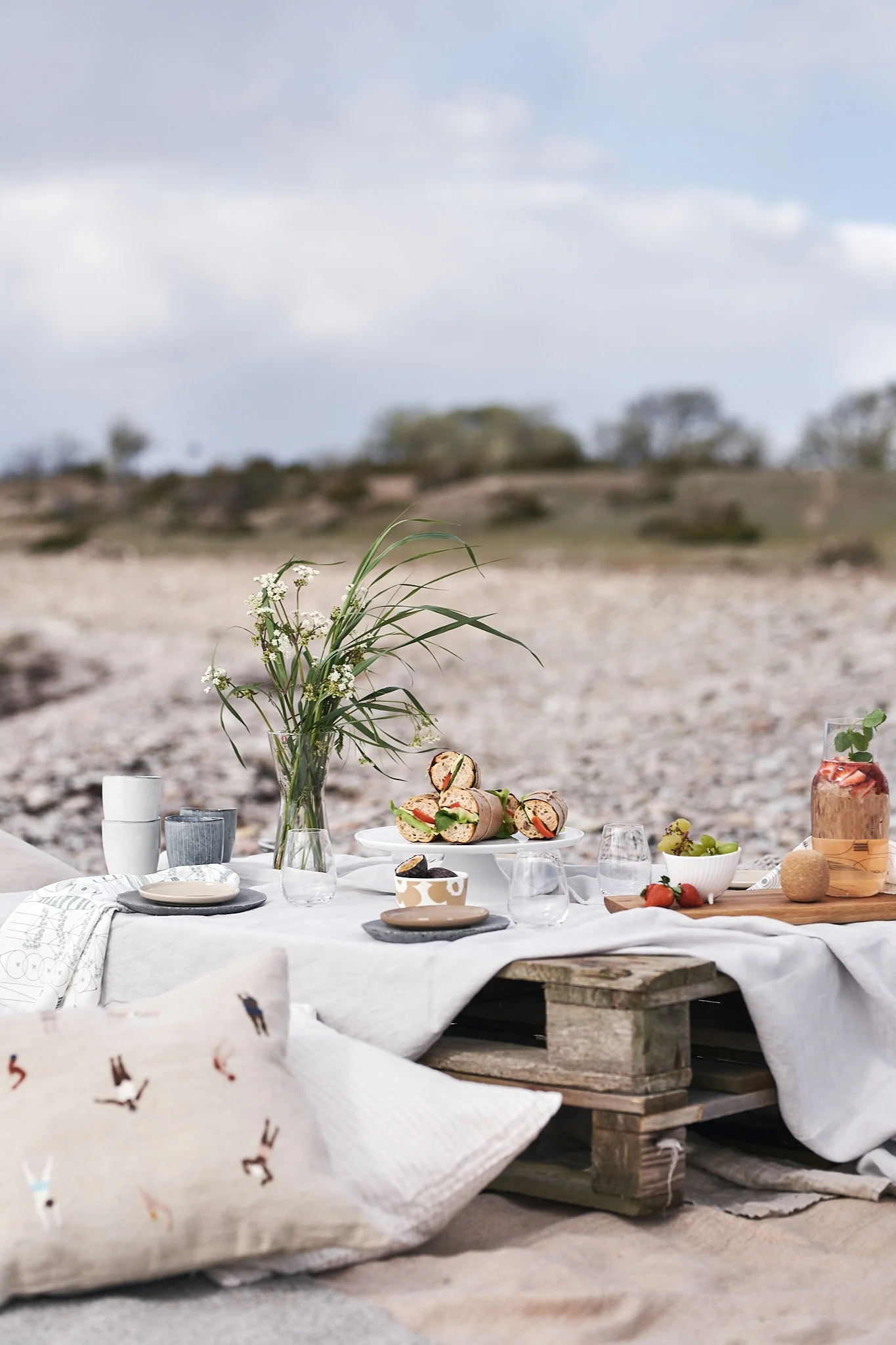 En lyxig picknick på stranden på lastpallar, med kuddar och enkel picknickmat.