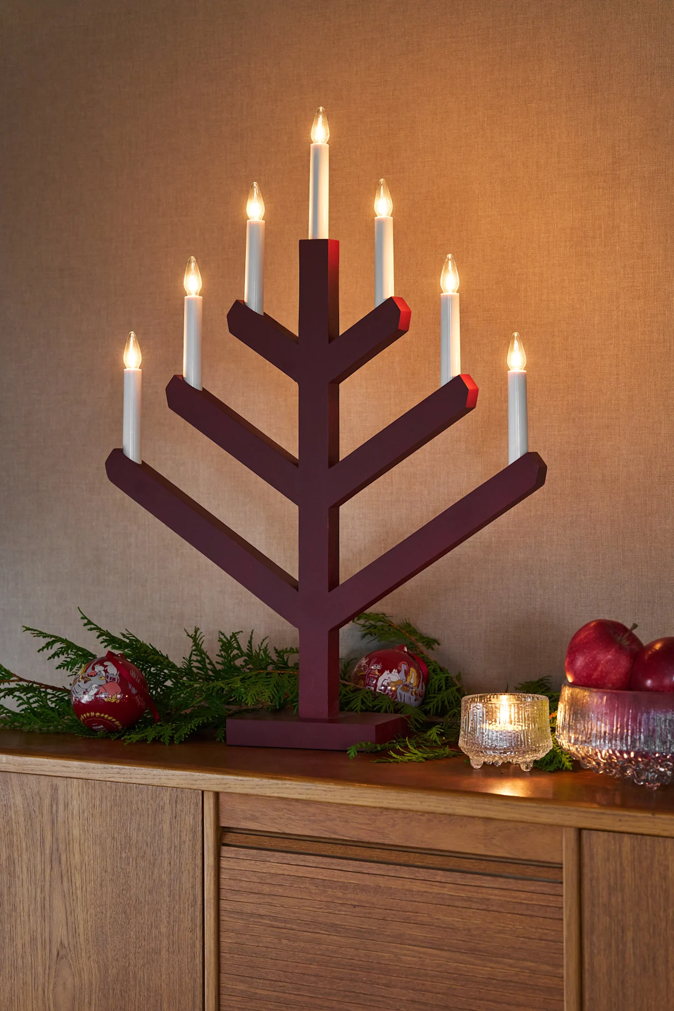 Första advent firas genom att tända Pine-adventsljusstaken från Scandi Living. Ljusstaken står vackert på en byrå tillsammans med ljuslykta och skål med äpplen från Ultima Thule. Julgranskulor och granris kompletterar den festliga dekorationen