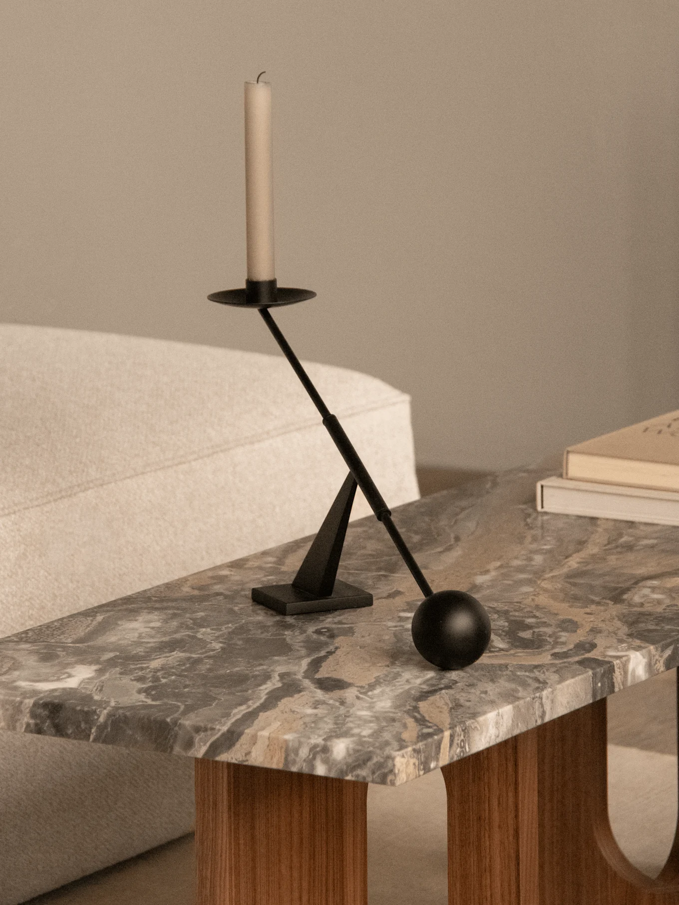 En svart modern ljusstake med ett vitt ljus på ett soffbord i marmor bredvid två böcker och en ljus soffa.
