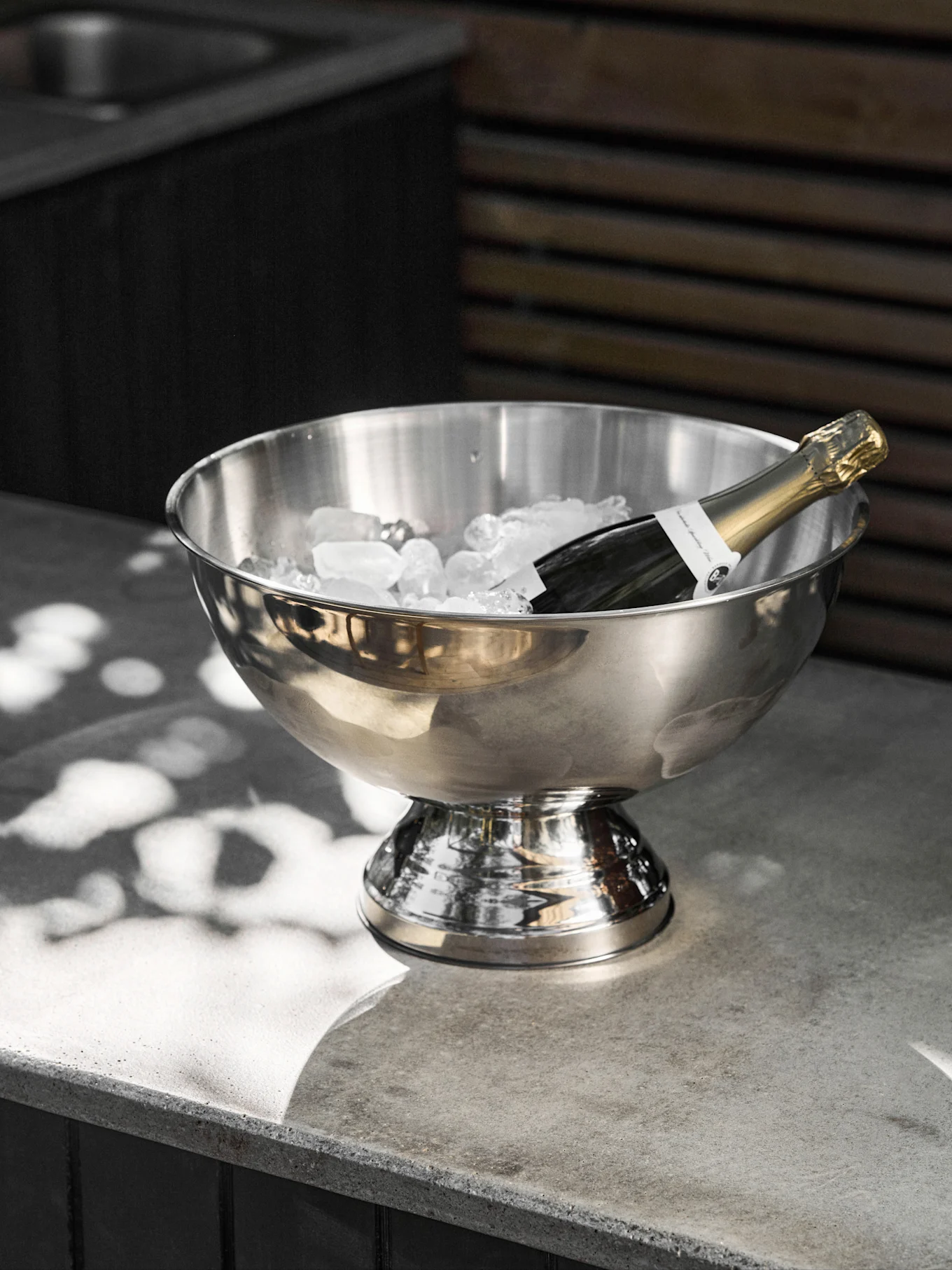 Champagneflaska kyls i en isbehållare av rostfritt stål på en betongyta.