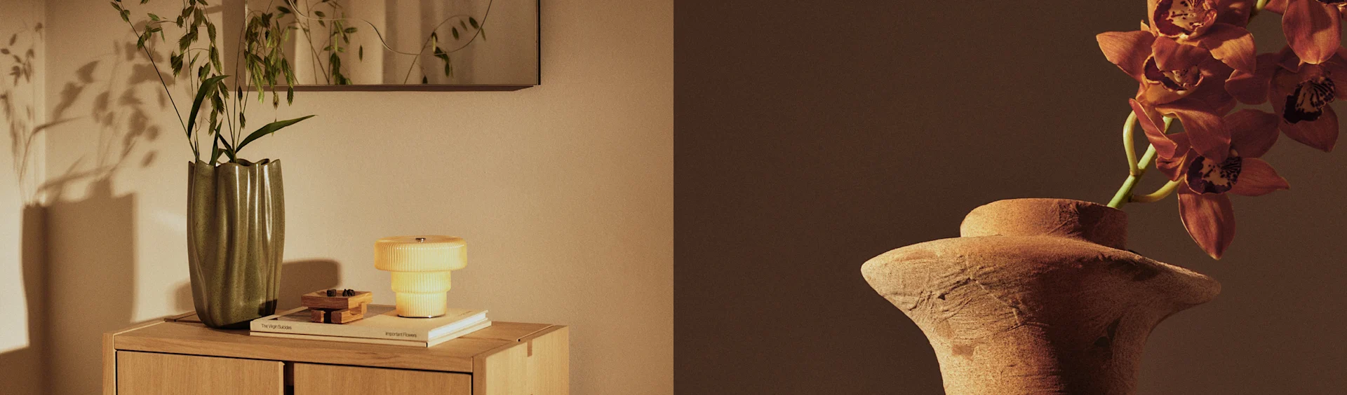 Två vaser visar växter, en grön vas med grönska på ett skåp bredvid en gul lampa, och en terrakottavas med orangea orkidéer.
