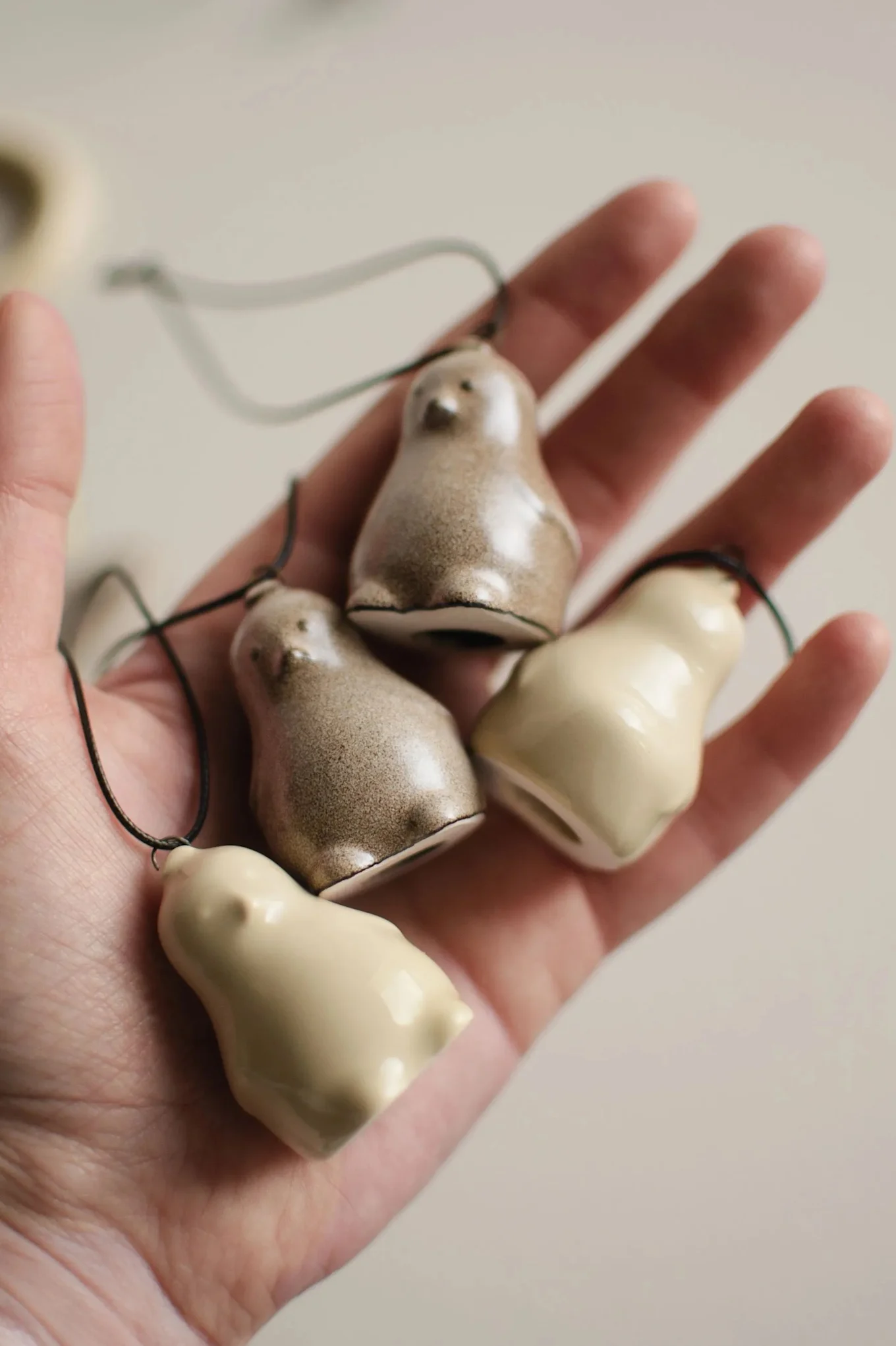 Hand håller fyra små keramiska fågelornament, två fläckiga bruna, två gräddvita, med snören.