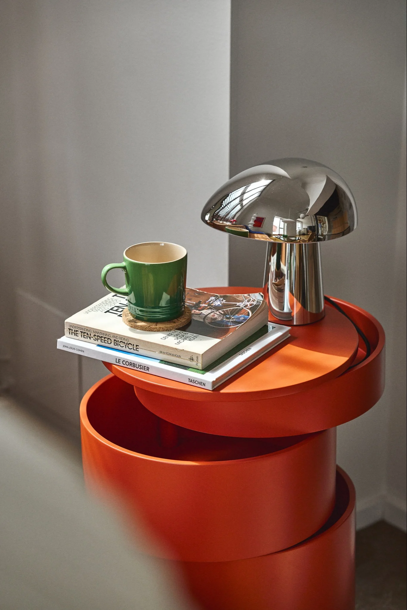 En Night Owl bordslampa i krom står på ett orange sidobord. Lampan tillhör en designklassiker. 