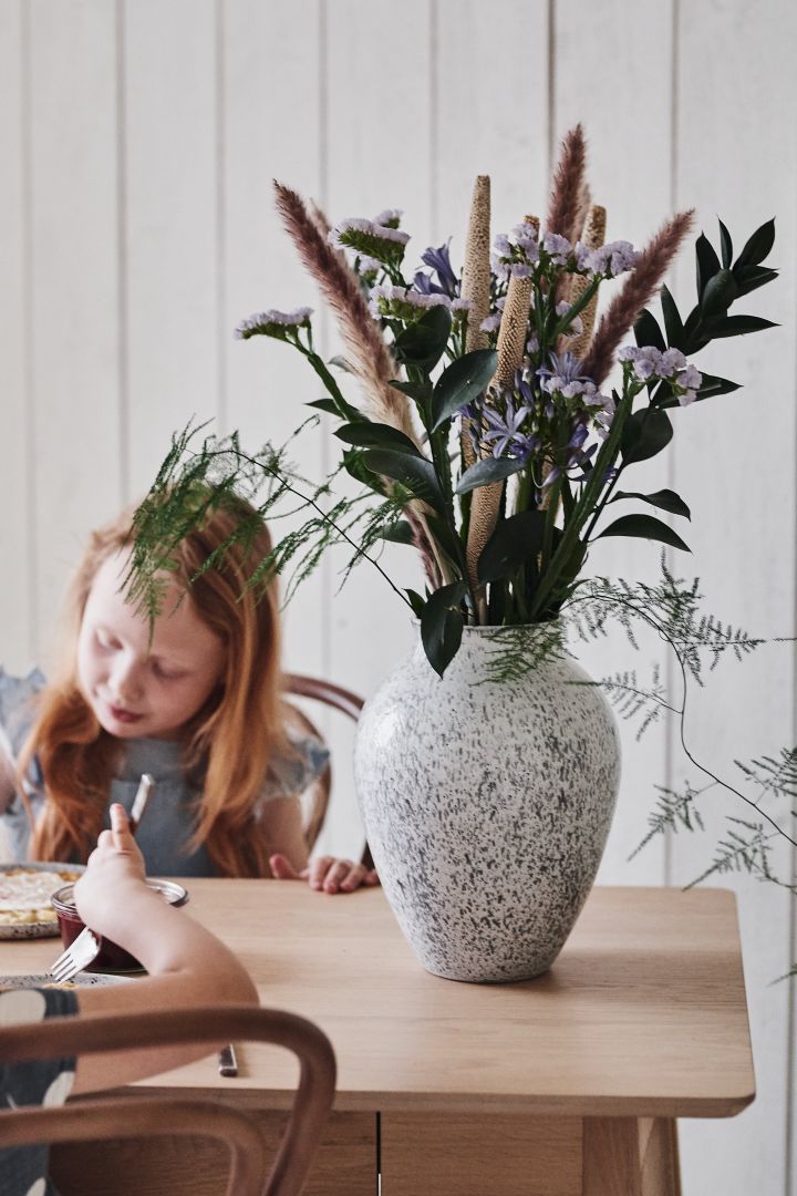 Hög vas i keramik från Kabstrup keramik fylld med torkade blommor från Blombruket står på matbordet. 