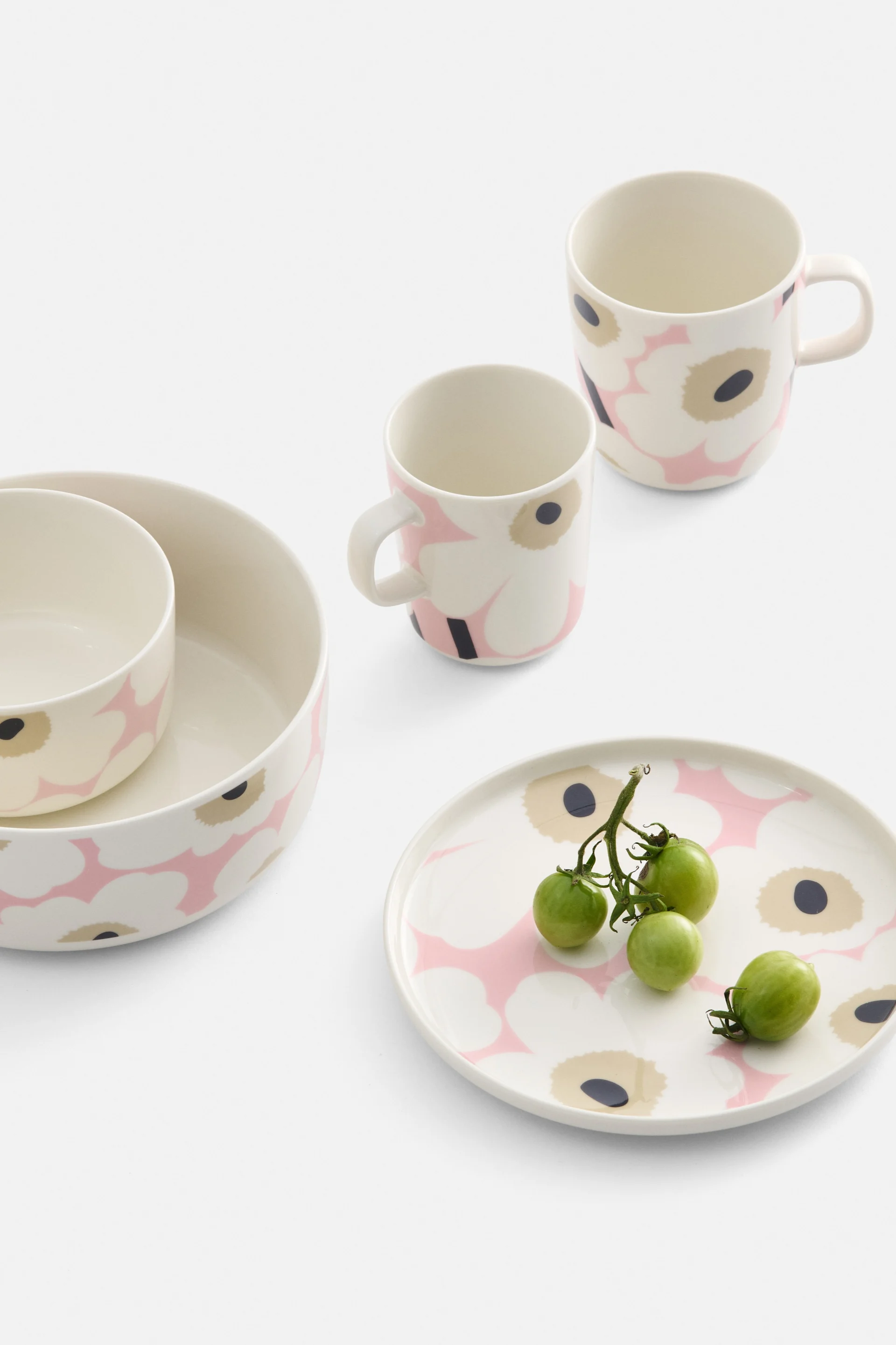 Gräddfärgat porslin med rosa och svart blommönster, inklusive två skålar, två muggar och en tallrik med gröna körsbärstomater.