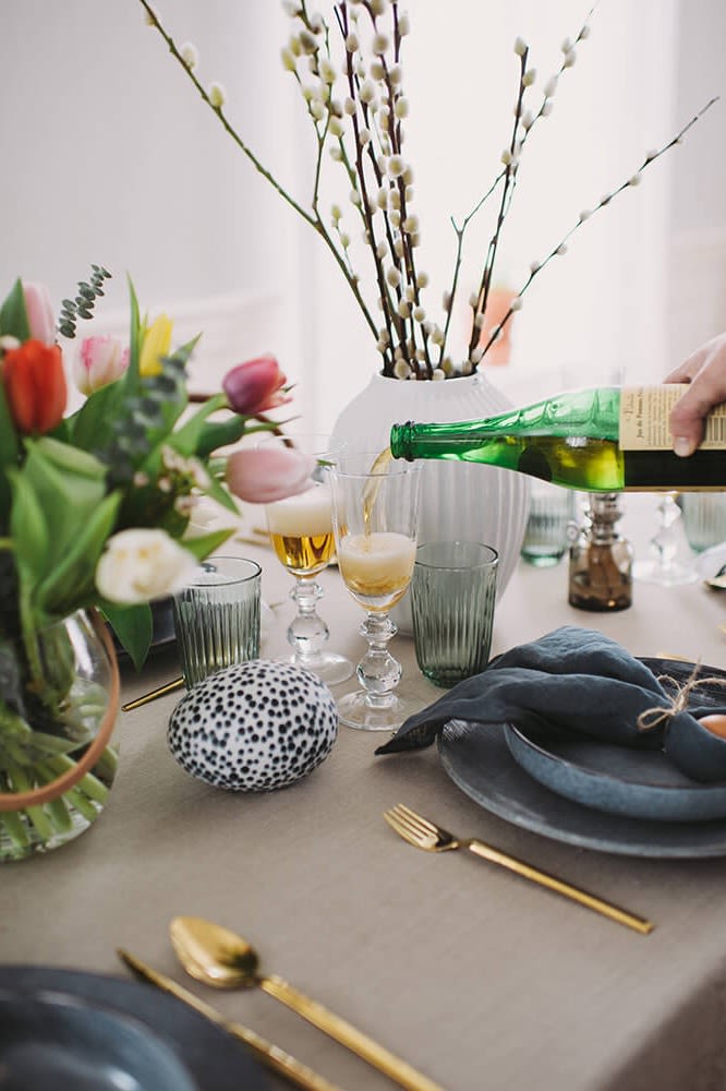 Matbord dukat för påsk med tulpaner och ägg på samt rustik porslin och servetter knutna som kaninöron.