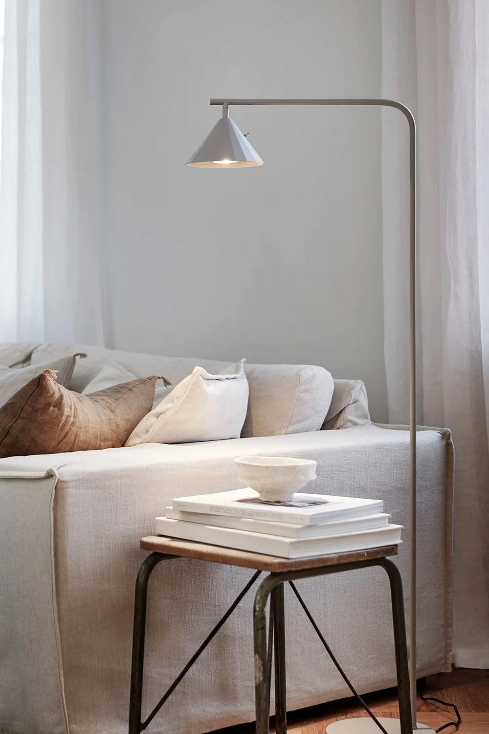 Ett mysigt vardagsrum med en ljus linnesoffa, golvlampa och ett sidobord med böcker och en skål.