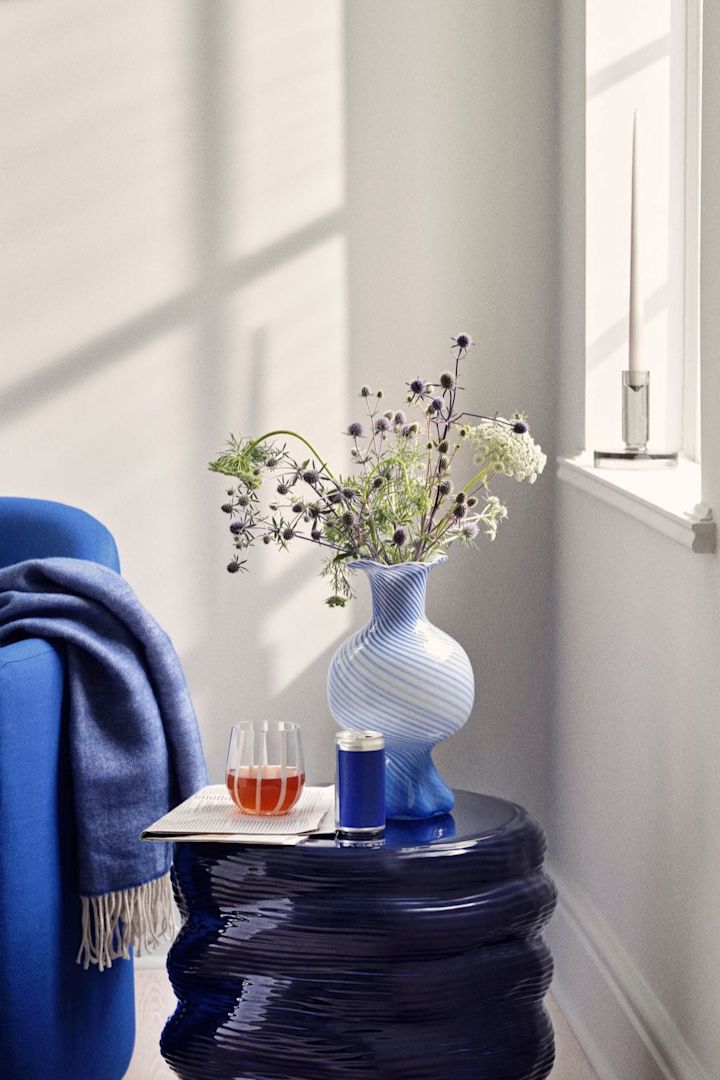 Mella vas i 30 cm och blå färg med randigt mönster står på ett sidobord bredvid en blå soffa, och innehåller en bukett med blommor.
