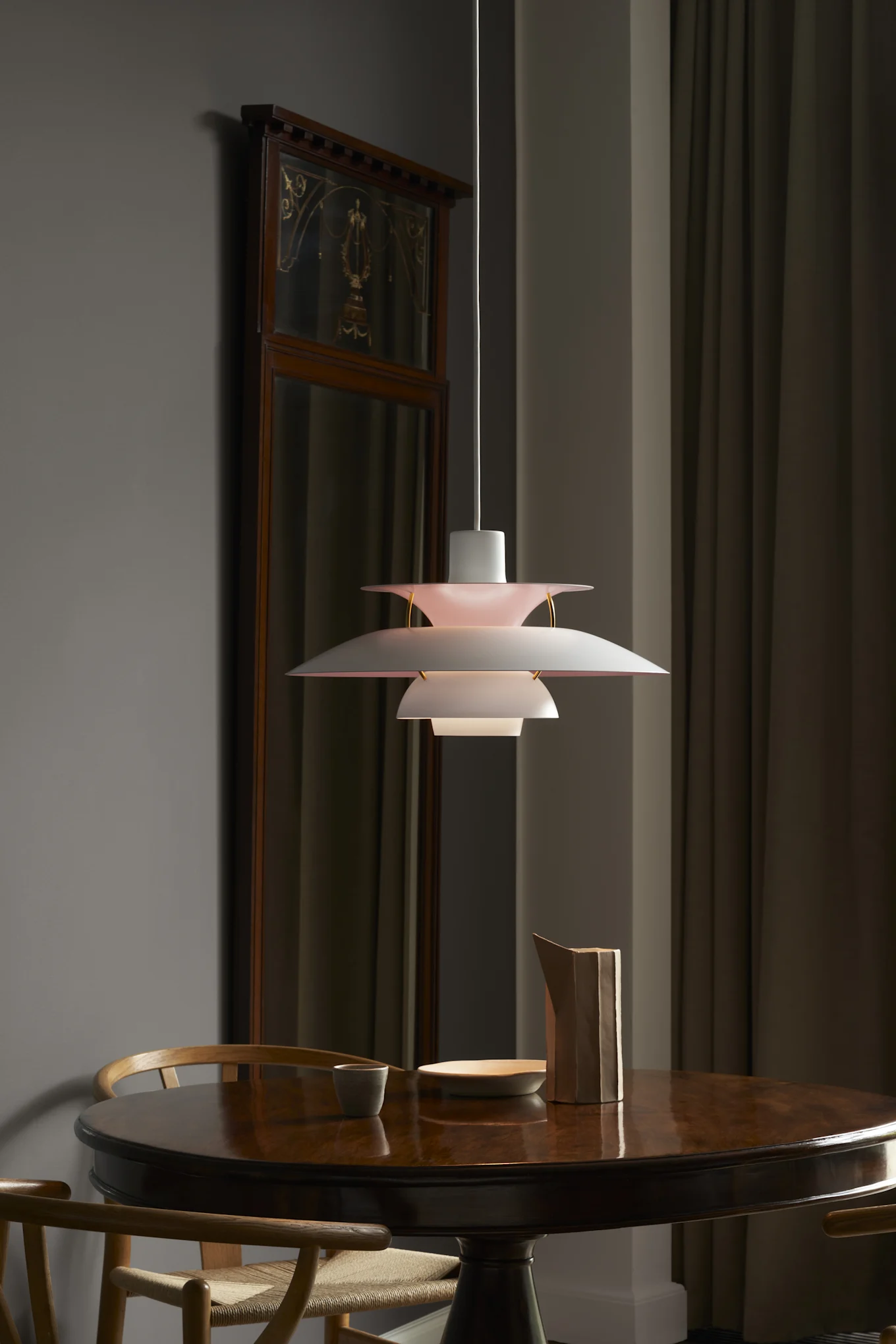 En vit lampa från Louis Poulsen, en dansk designklassiker, hänger elegant över matbordet där tre Y-stolar samlas runt.