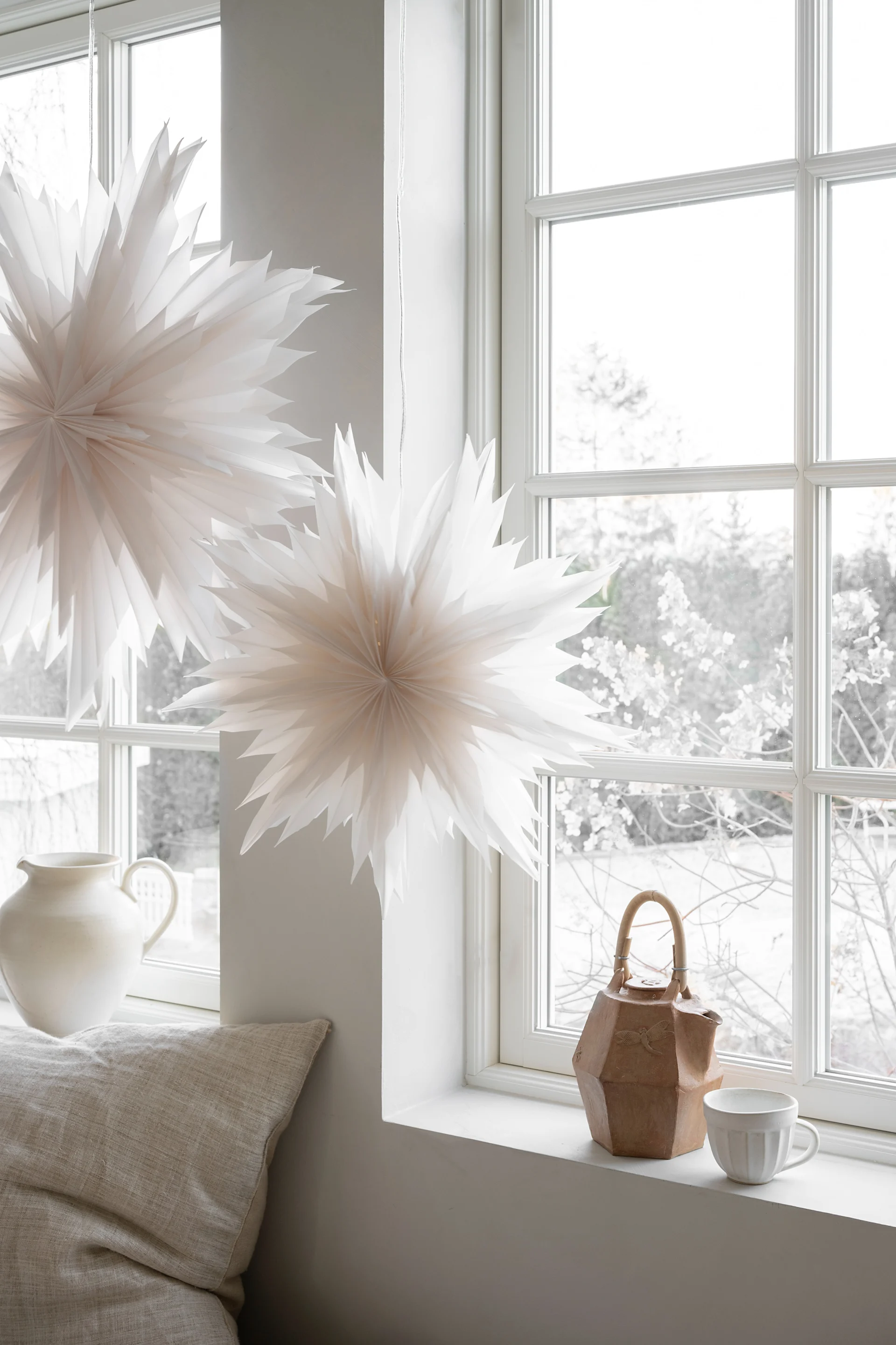 Dekorativa pappersstjärnor och lagerformade blomsterornament utställda bland mossiga skogsträd.