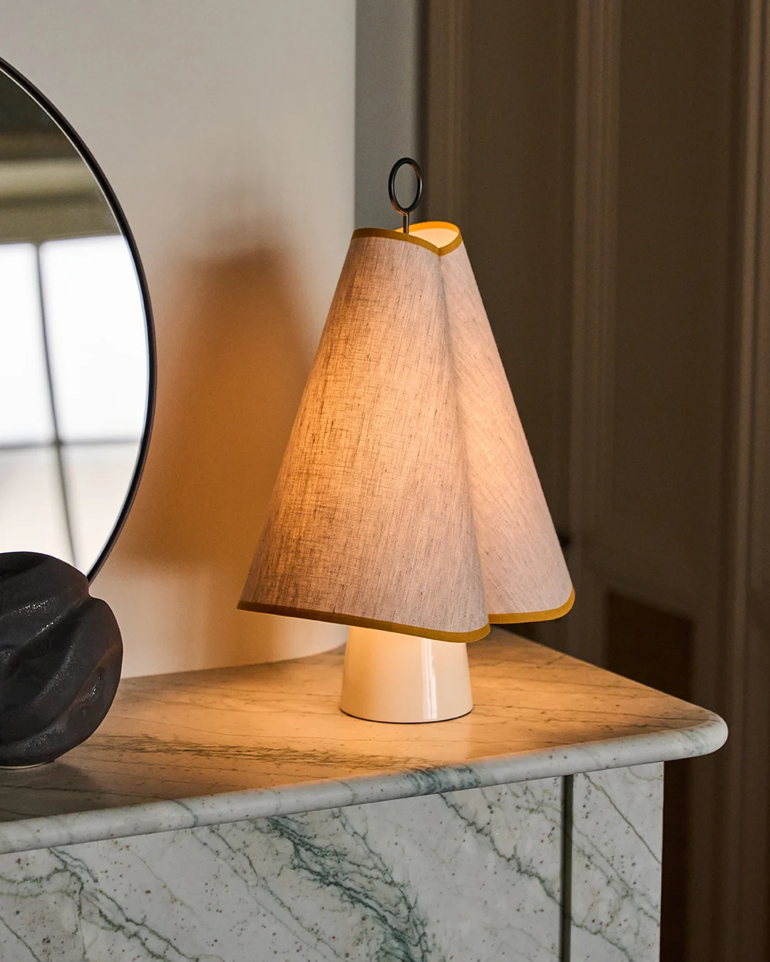 En unik bordslampa med dubbel konisk tygskärm kantad i gult, som kastar ett varmt sken på en grön marmorskiva.