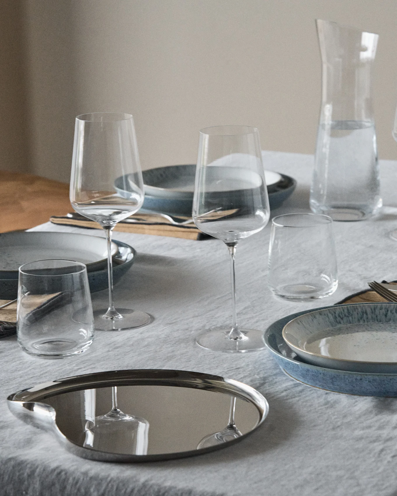 Ett dukat bord med blå och spräckliga tallrikar, vinglas, dricksglas, en vattenkaraff och en reflekterande oval bricka.