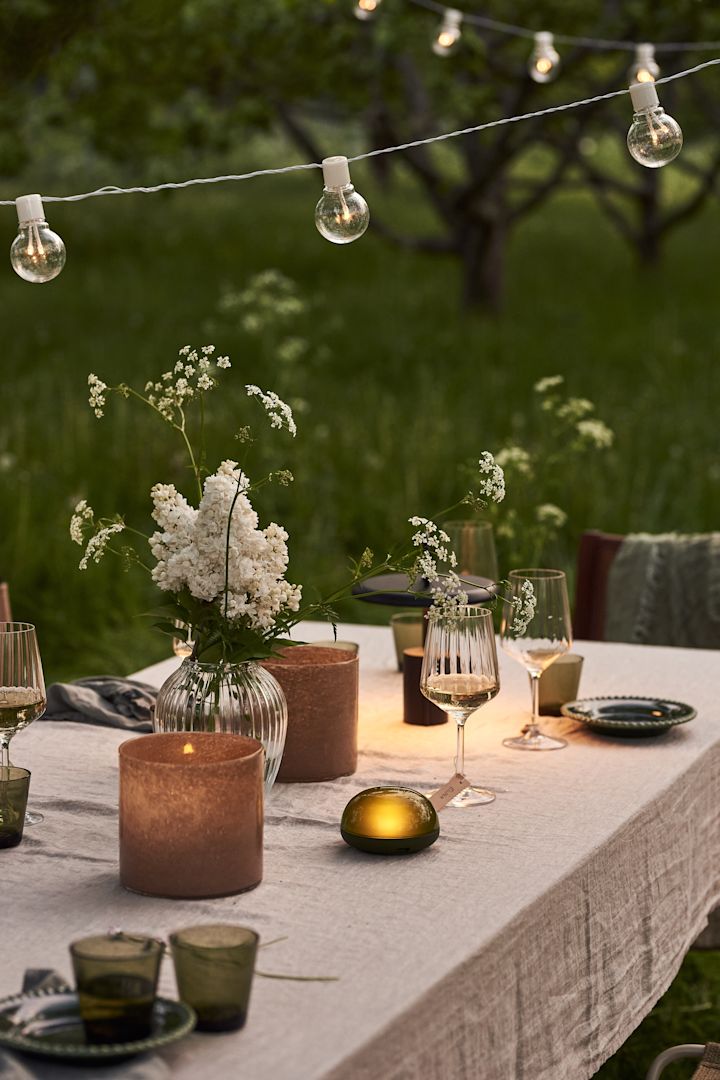 En sommardukning i trädgården är inte komplett utan portabel belysning. Här ser du Soft Spot portabla LED-lampa från Rosendahl och Star Trading ljusslinga.
