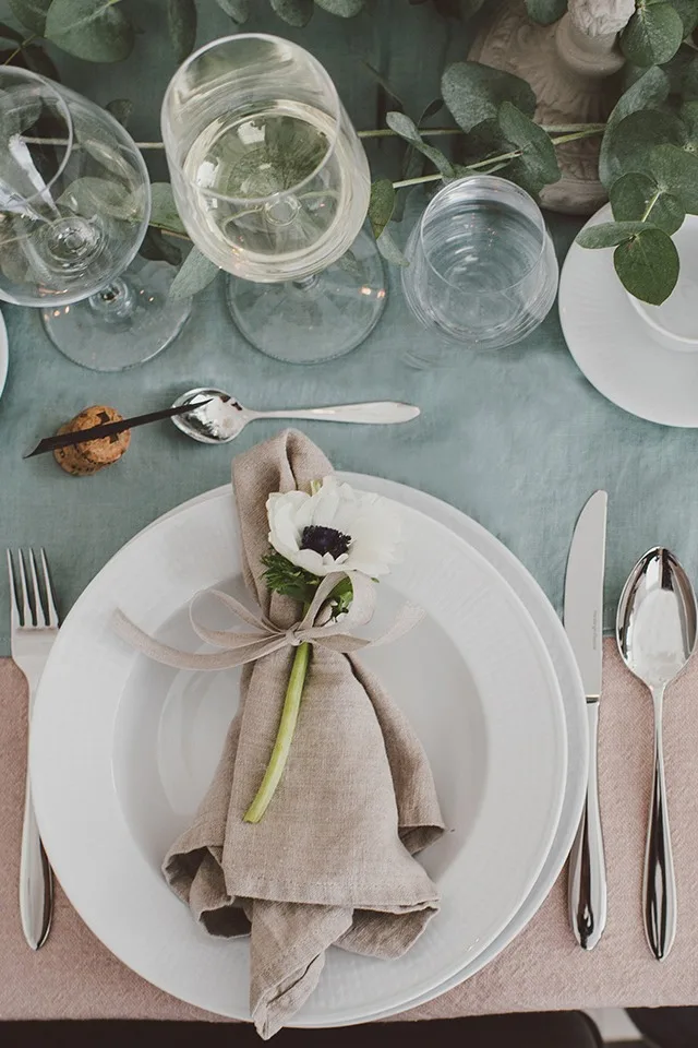 Beige linneservett knuten med dekorativt band och en levande blomma på en festlig dukning med Swedish Grace.
