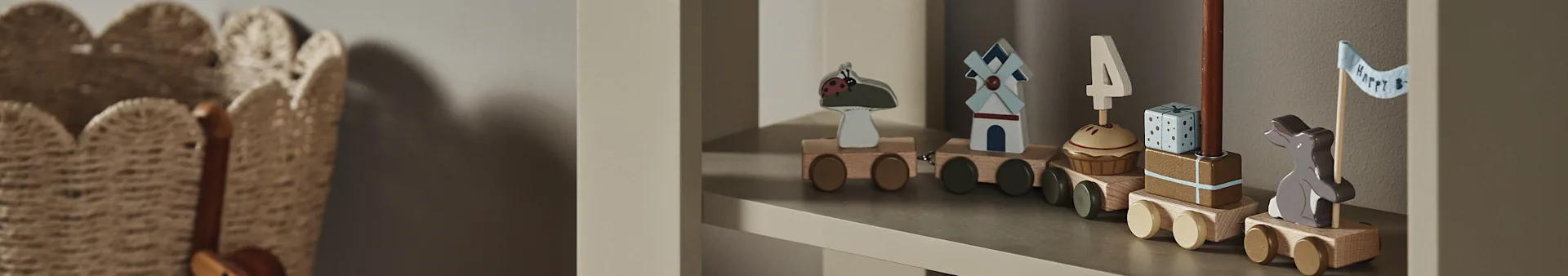 Ett träleksakståg på en hylla, med vagnar med en nyckelpiga, väderkvarn, cupcake med "4"-ljus, present och en kanin med en "Happy B"-flagga.