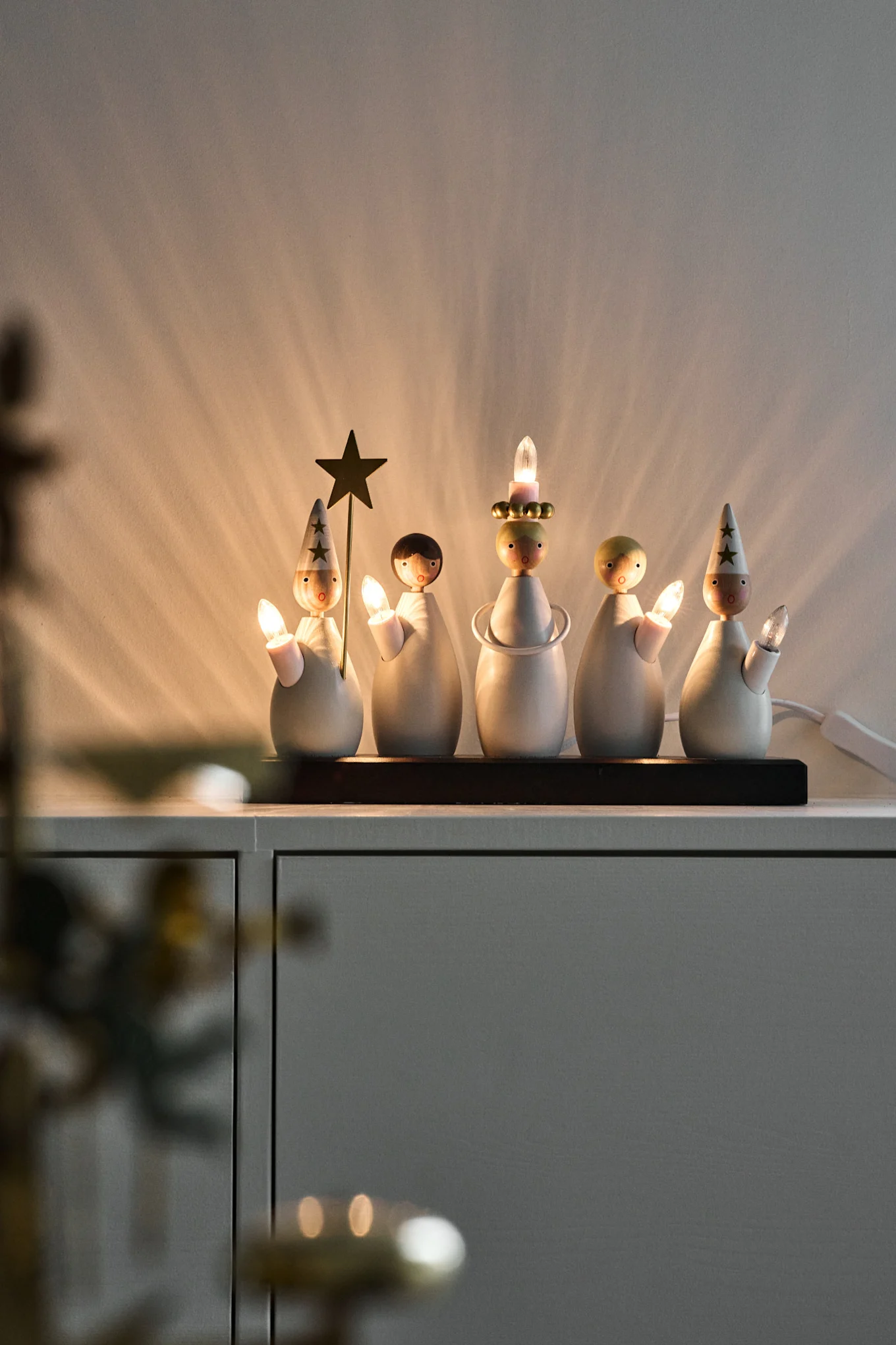 En adventsljusstake som föreställer ett luciatåg står på en byrå och lyser.