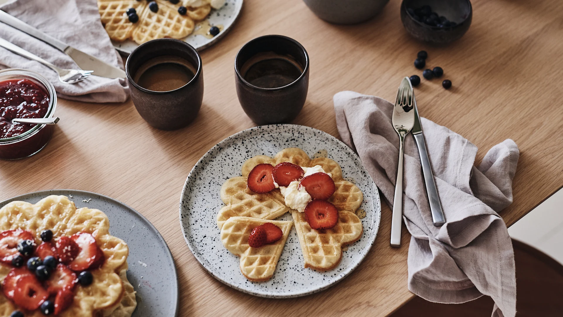 Ledig dukning med våfflor på rustik tallrik och ledigt lagd linneservett på bordet.