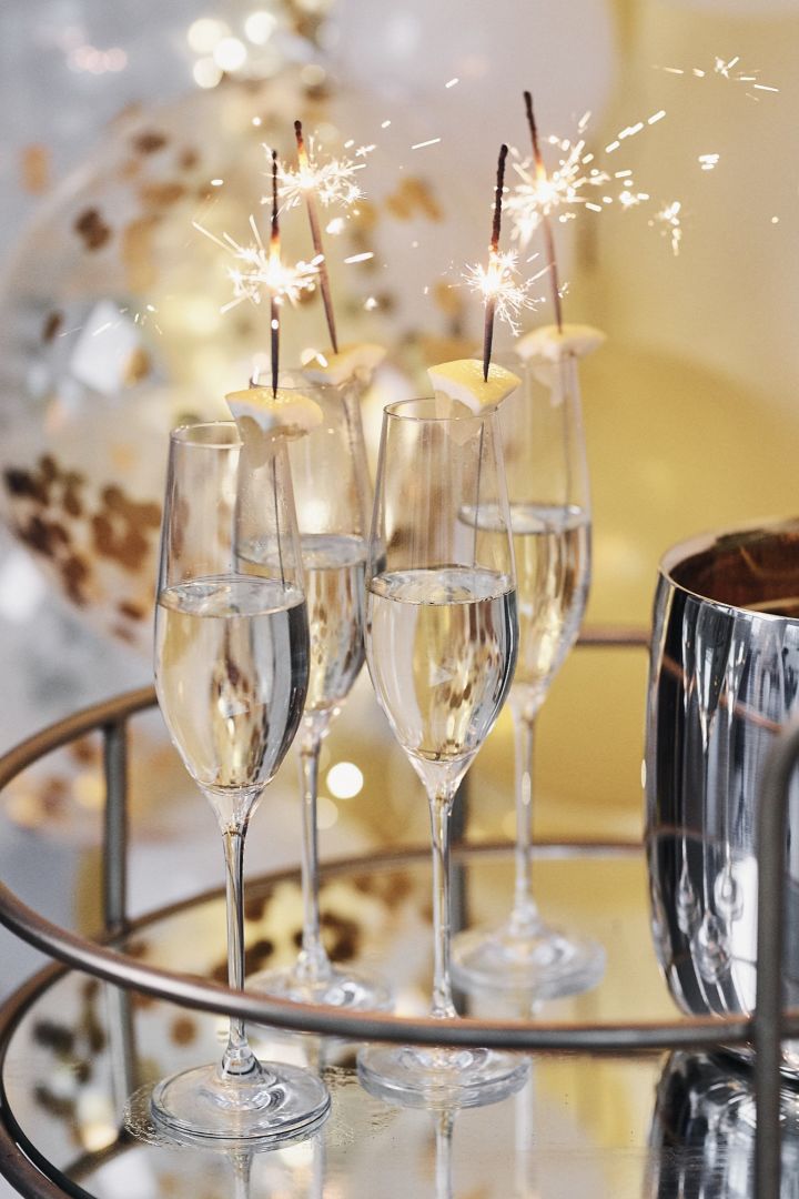 Nyårsdrink med bubbel serverat i höga champagneglas med sprakande tomtebloss. 