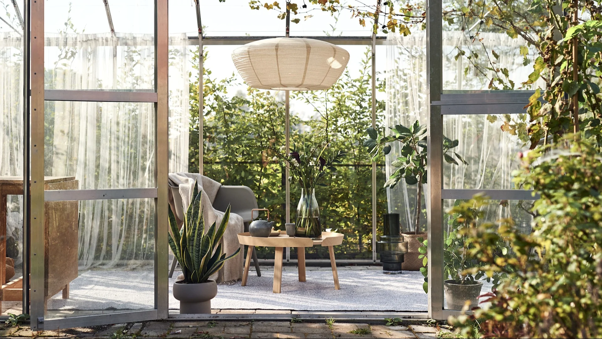 Utomhusmatta: Här ser du ett växthus som har förvandlats till ett mysigt vardagsrum, med en pendellampa, en stol, ett sidobord och en stor matta utomhus.