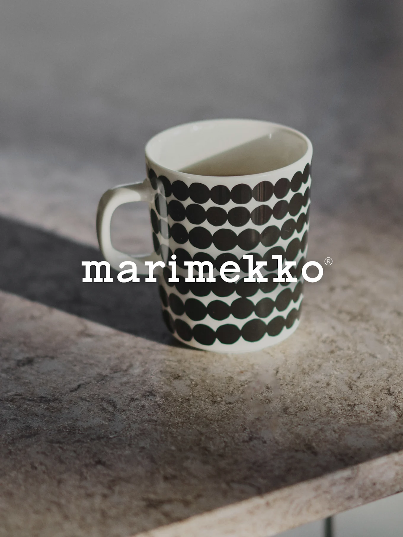 Vit Marimekko-mugg med svart prickmönster på en grå yta.