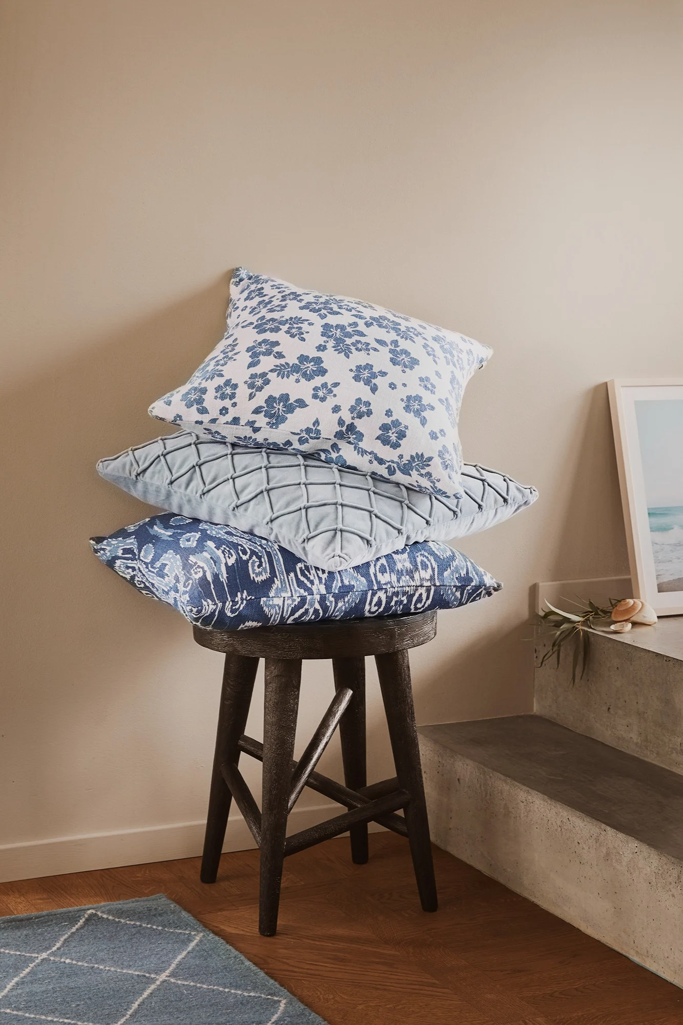 Kuddfodral från Chhatwal & Jonsson i tre olika mönster i blå färg ligger staplade på en stol i mörkt trä. 