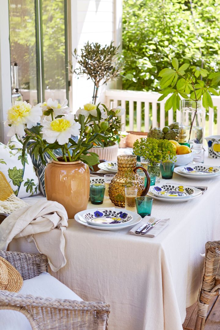 Duka till midsommar utifrån en medelhavsinspirerad stil med gula detaljer, pioner på bordet och gröna glas från Iittala. 
