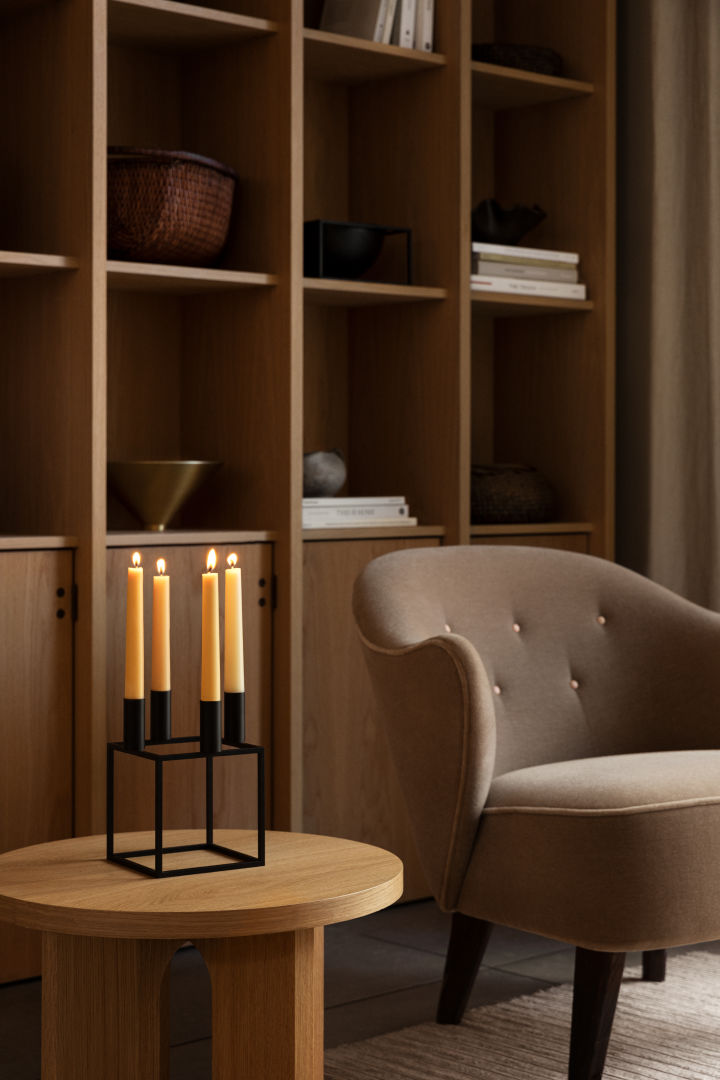 Kubus ljusstake 4 från by lassen är numera en del av varumärket Audo Copenhagen - här på ett soffbord i trä med bokhylla bakom. 