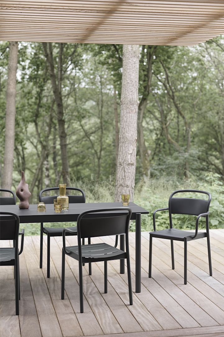 En täckt träterrass med ett bord och stolar i svart från Linear-kollektionen från Muuto.