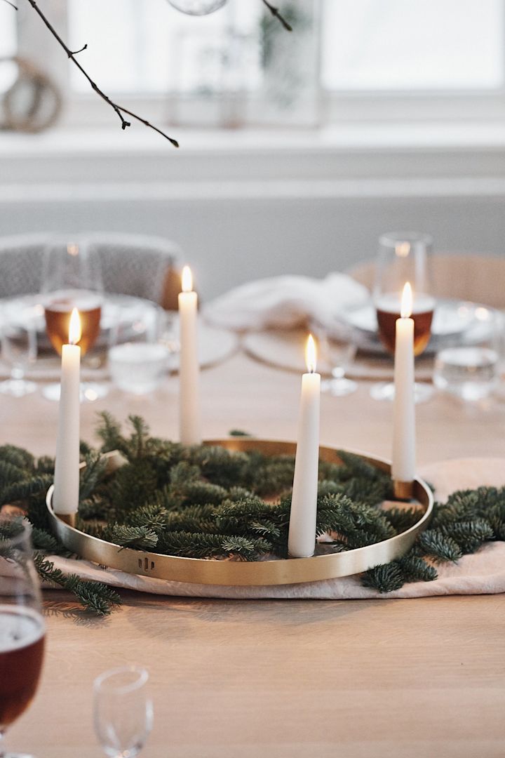 Granris och en rund ljusstake i mässing med vita ljus står i mitten av en vit juldukning och sprider stämning. 