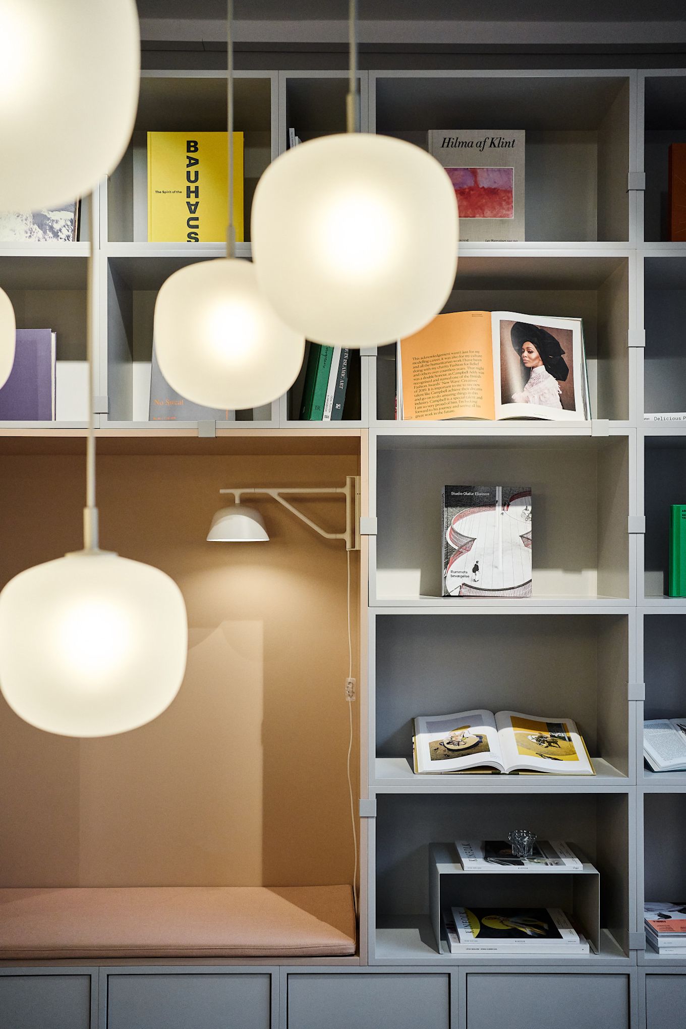 En prydlig hylla inredd med böcker, med flera Rime-pendellampor från Muuto hängande i förgrunden.