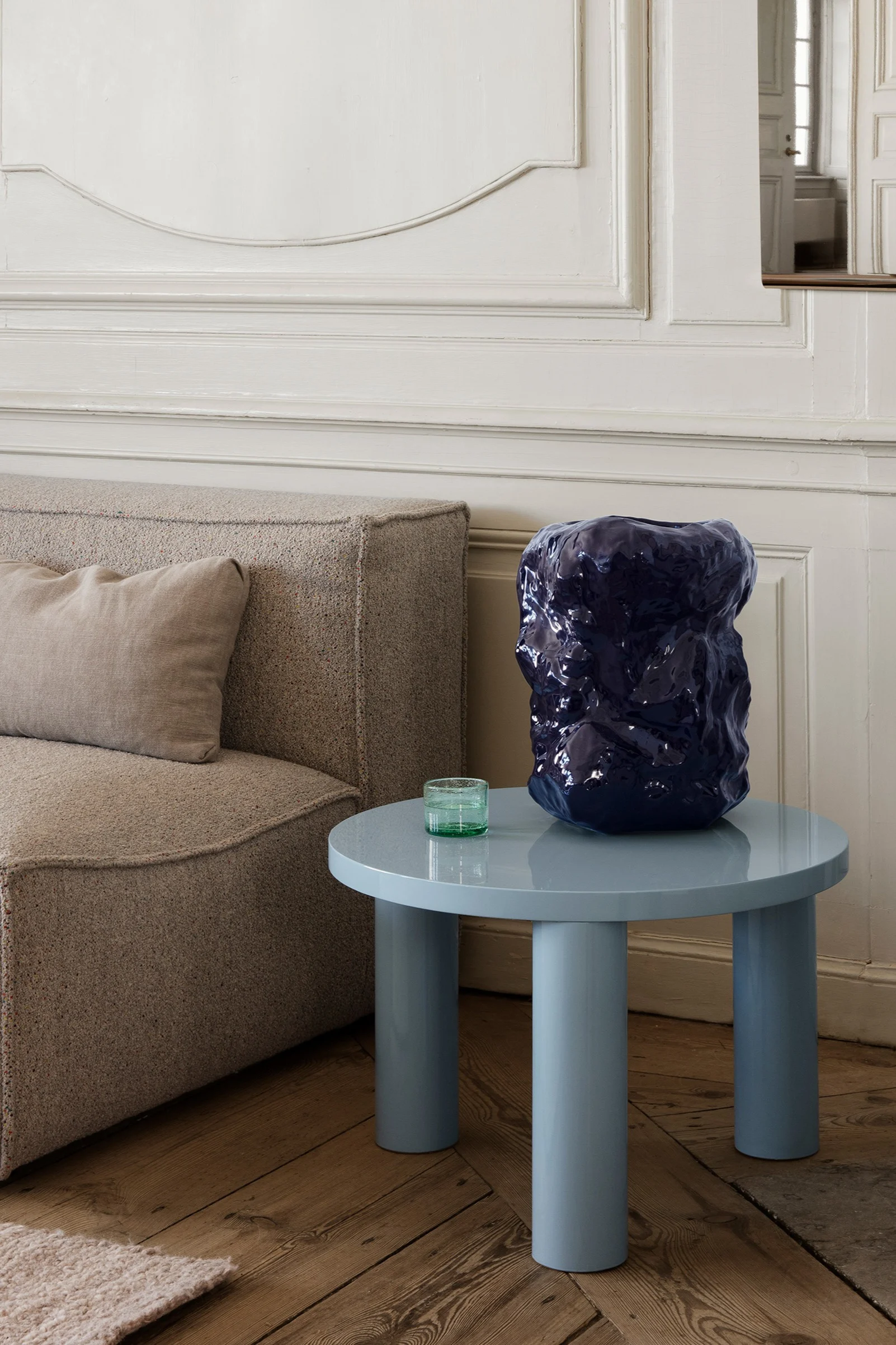 Post soffbord från Ferm Living i en ljusblå färg står på ett trägolv bredvid en grå soffa.