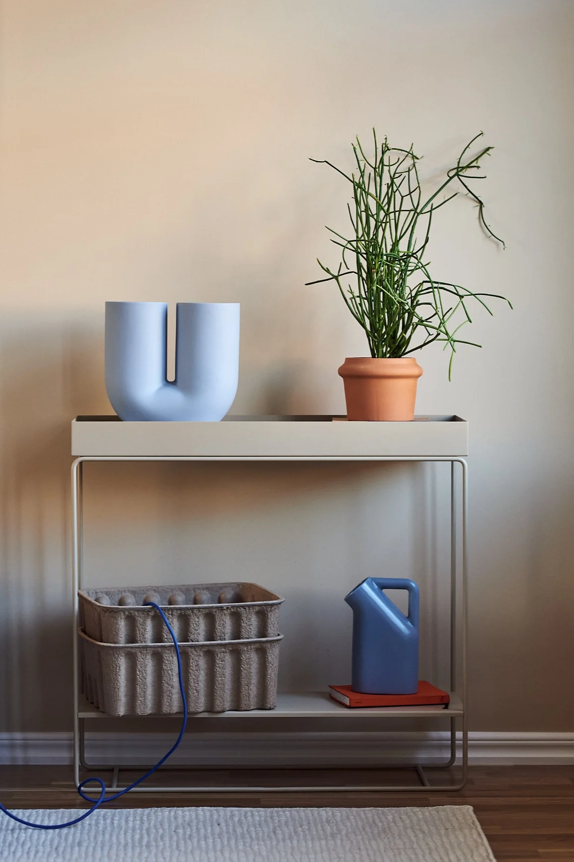Inred ditt vardagsrum med beige inredning i kombination med färg för ett livfullt intryck i ditt hem. Här ser du mångsidiga och praktiska Plant Box konsolbord från Ferm Living i beigt tillsammans med blå Kink vas och Tub kanna från Muuto.