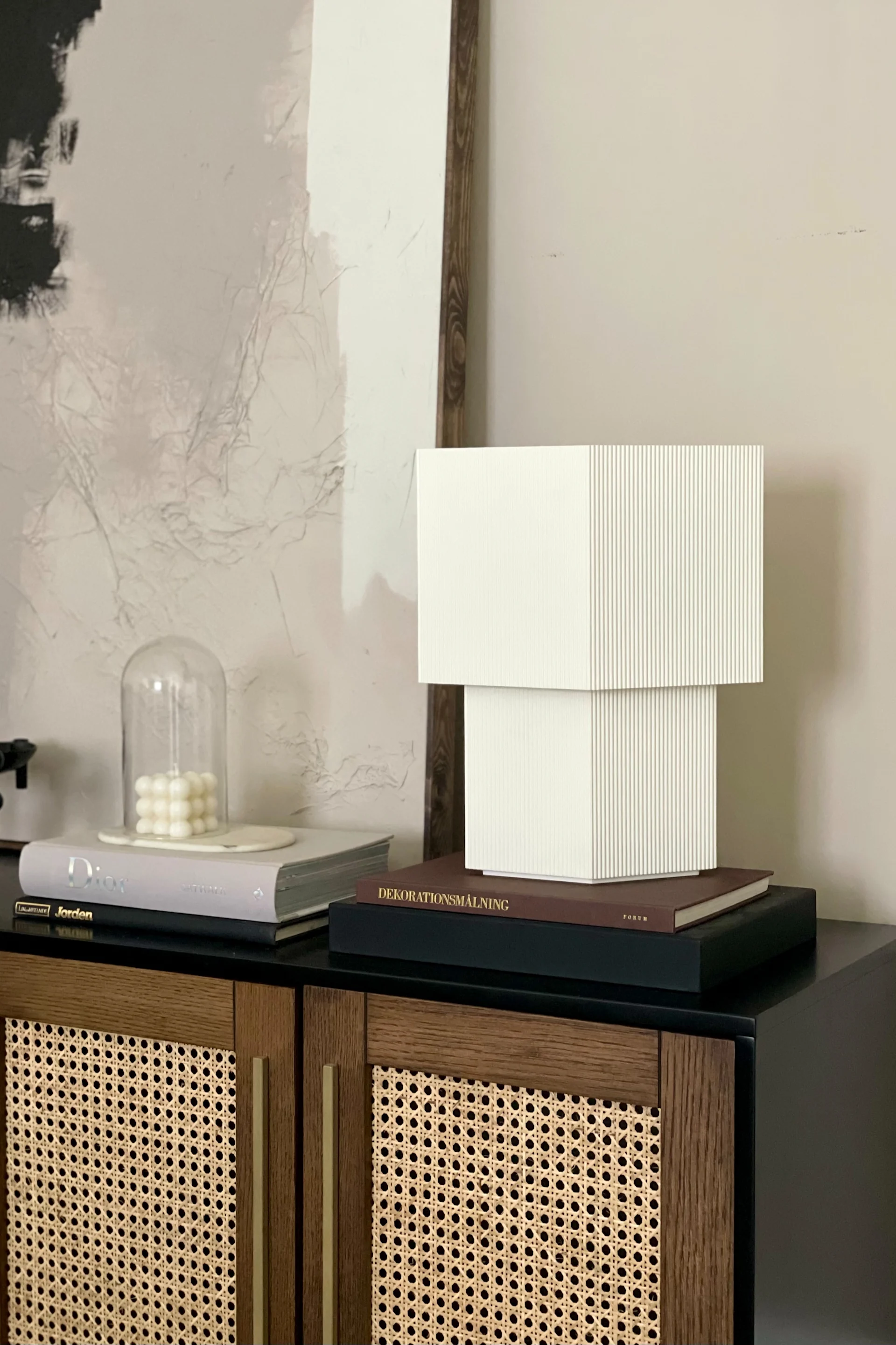 Stilleben inom inredning kan tolkas på flera sätt - här med vit, japandi-inspirerad bordslampa, böcker och ljuslyktor.