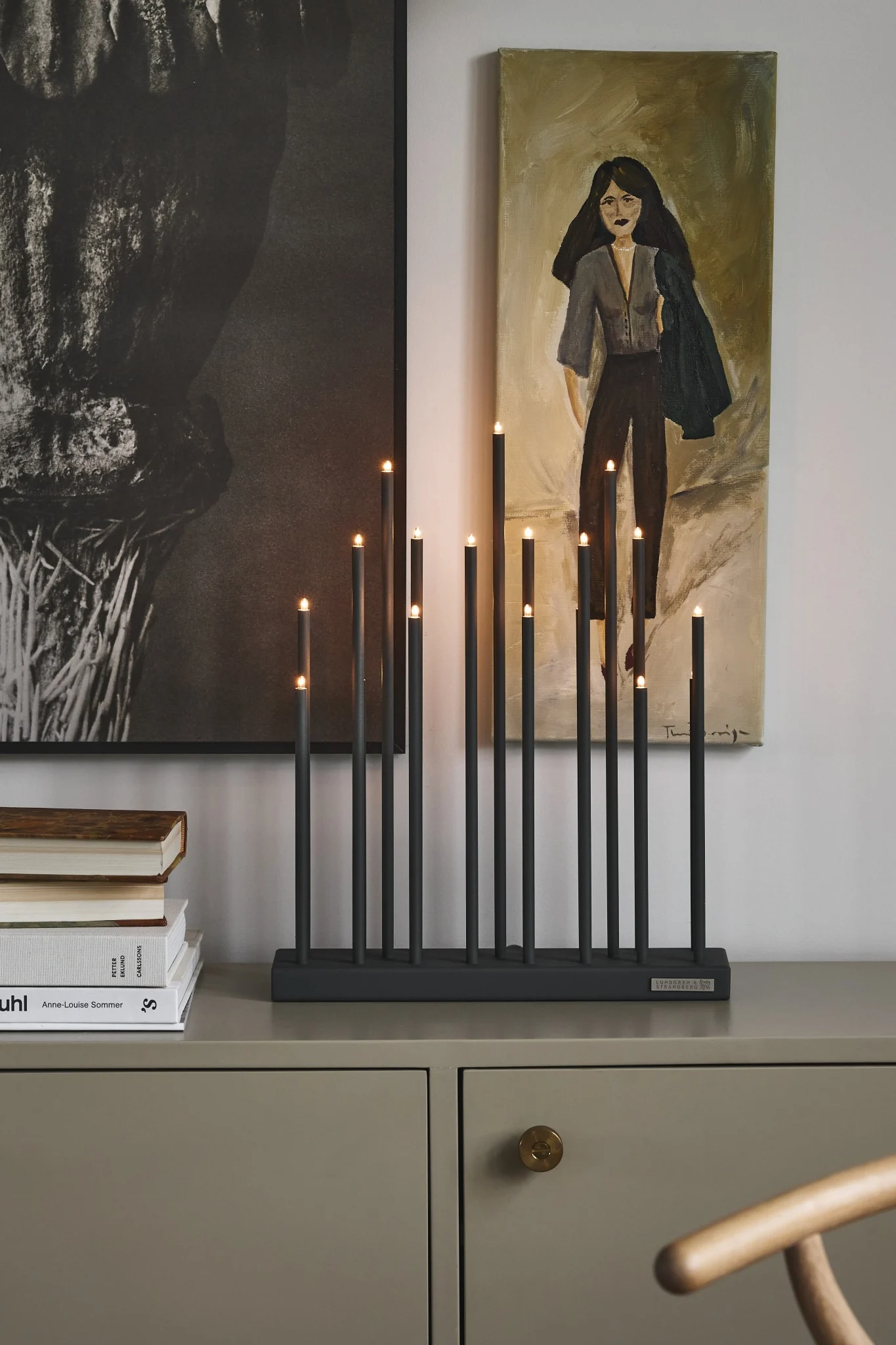 Elflugan adventsljusstake står på en byrå och lyser med rustika tavlor i bakgrunden. 