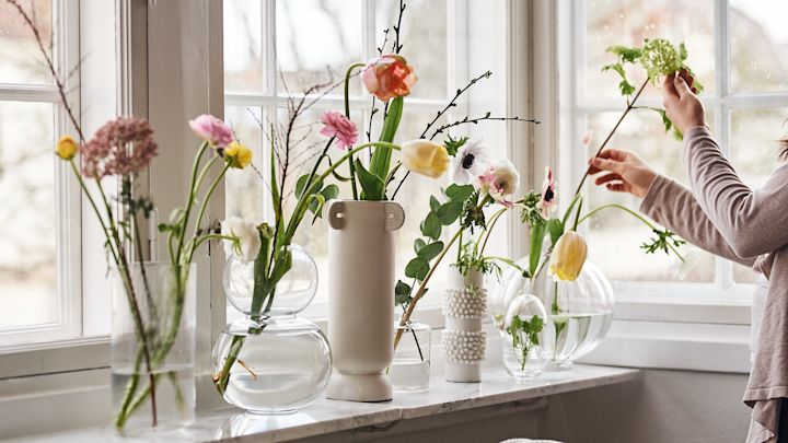 Vaser i klarglas med snittblommor i står på fönsterbrädan. 