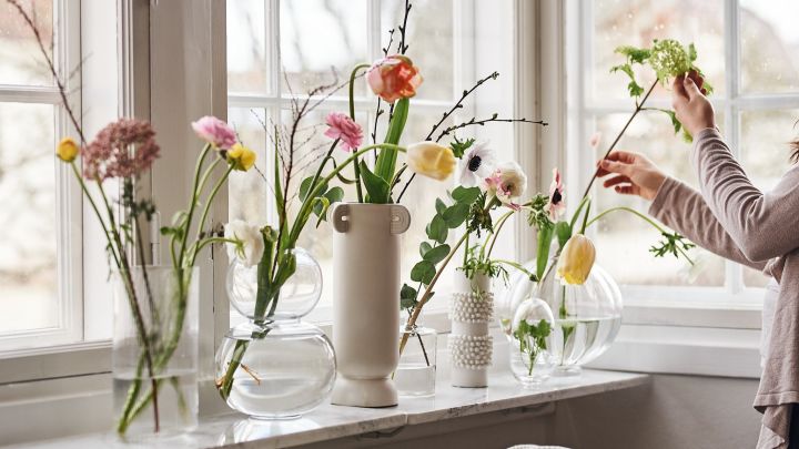 Vaser i klarglas med snittblommor i står på fönsterbrädan. 