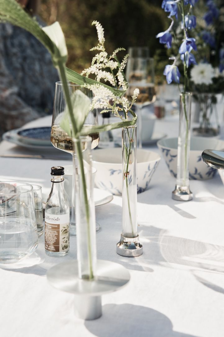 Glasvaser i olika storlekar och stilar med vita och blåa blommor matchar den blåvita midsommardukningen och skapar känslan av en sommaräng.