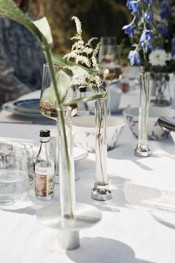 Glasvaser i olika storlekar och stilar med vita och blåa blommor matchar en blåvit midsommardukning och skapar känslan av en sommaräng.