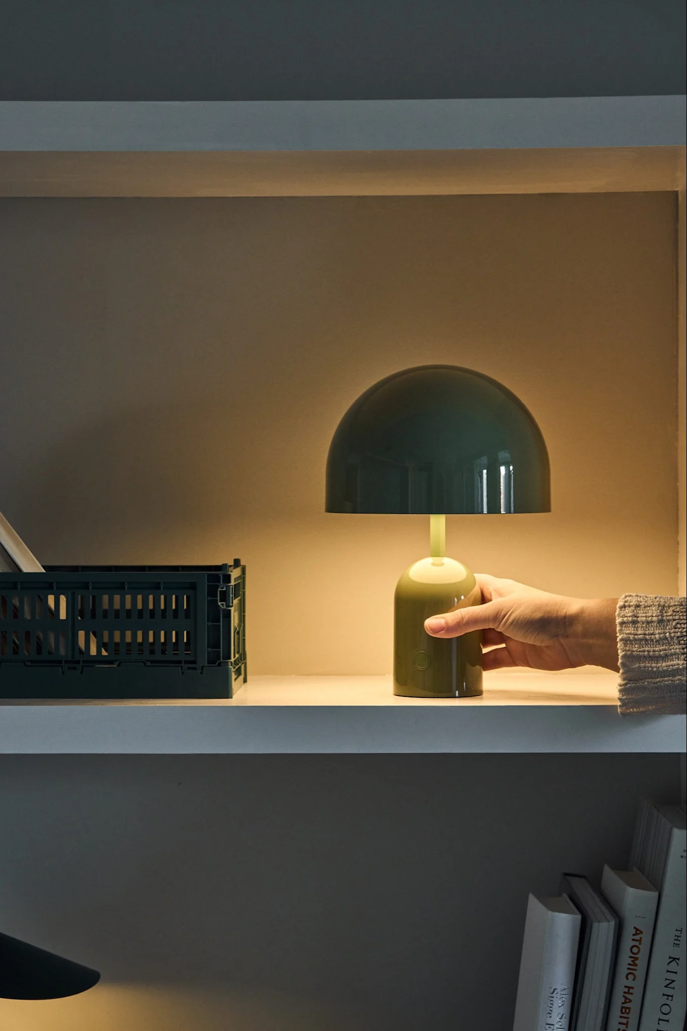Bell grön portabla lampa från Tom Dixon tänds av en hand i på en hylla. 