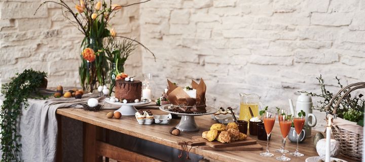 En rustik påskbuffé står uppdukad i lantlig miljö och långbordet är fullt av olika påskdesserter som chokladtårta serverad på Swedish Grace tårtfat. 