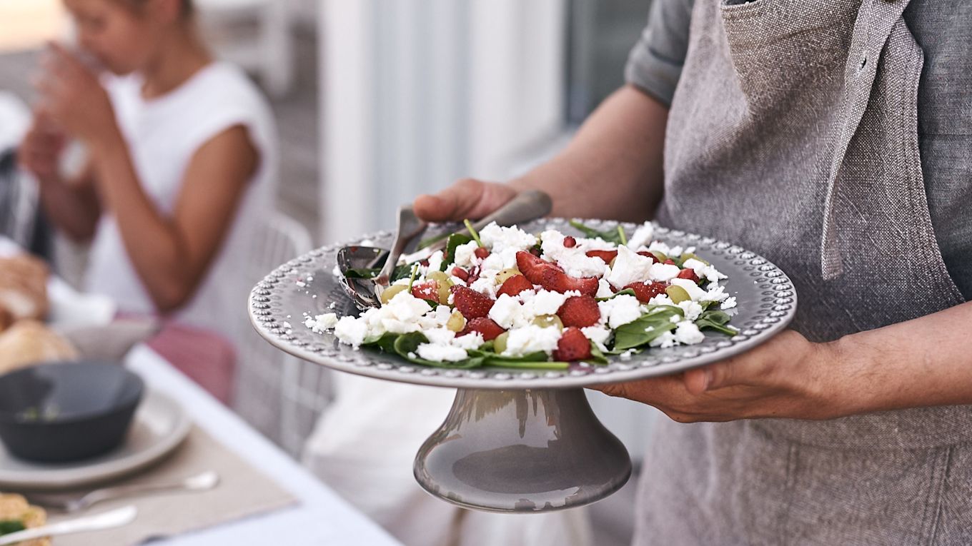 På sommardukningen står ett tårtfat från PotteryJo på bordet där en härlig somrig sallad gjord på jordgubbar och fetaost står serverad. 