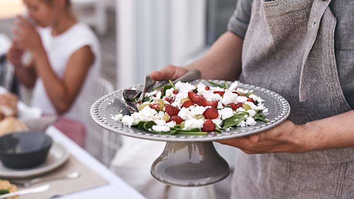 På sommardukningen står ett tårtfat från PotteryJo på bordet där en härlig somrig sallad gjord på jordgubbar och fetaost står serverad. 