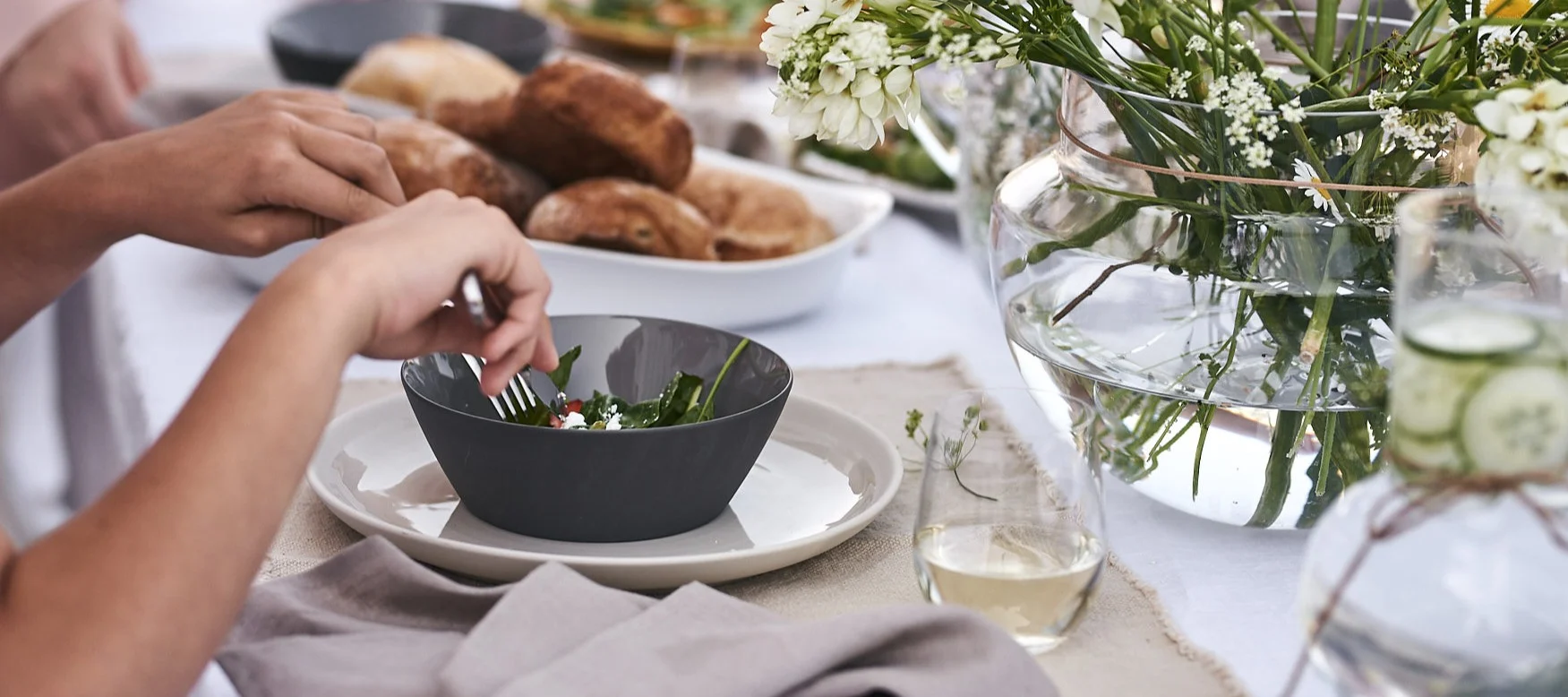 Det är uppdukat för sommarlunch med en sval sommardukning med tallrik och skål i stengods på vit linneduk.