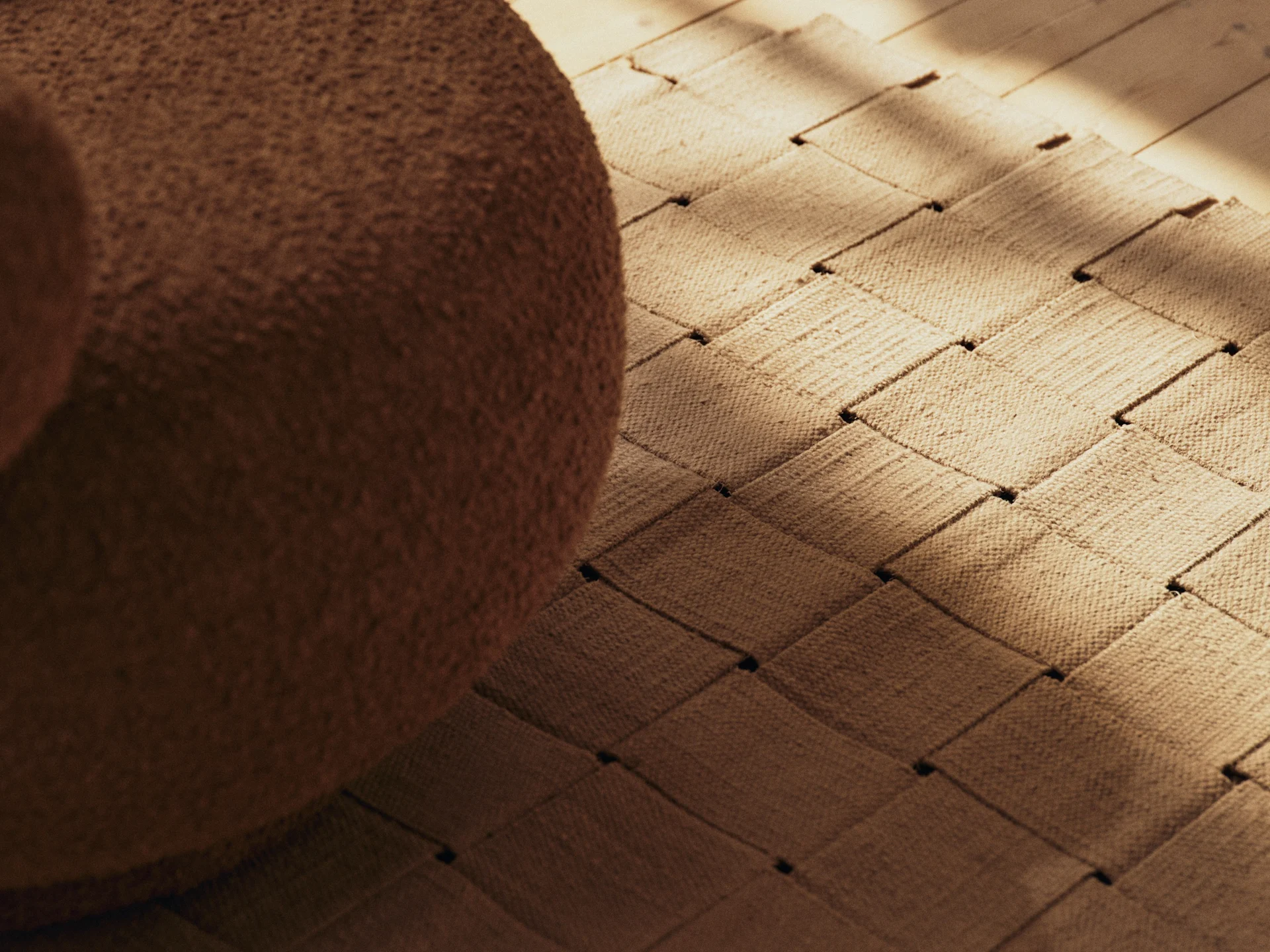 Bruna bouclé-möbler, en vävd matta och ett trägolv med solbelysta skuggor.