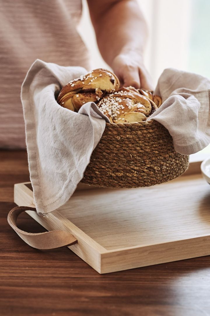 Fika förbereds i köket med kaffebröd i en brödkorg och kaffekoppar på en träbricka. 